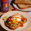 Avocado toast with poached egg and Fumami fermented Chili Ketchup on a plate, with a bottle of irresistible Fumami hot sauce in the background.
