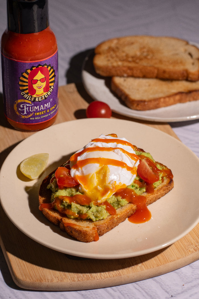 Avocado toast with poached egg and Fumami fermented Chili Ketchup on a plate, with a bottle of irresistible Fumami hot sauce in the background.