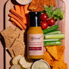 Fumami Creamy Salsa sauce bottle on a charcuterie board with chips, vegetables, and crackers