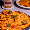 Nacho dish with Fumami creamy salsa sauce, tortilla chips, and a bottle of Fumami creamy salsa on a white surface.
