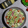 Delicious salad with cucumbers, tomatoes, and onions and feta cheese drizzled with a Fumami fermented creamy mint sauce, next to a bottle of Creamy Mint.