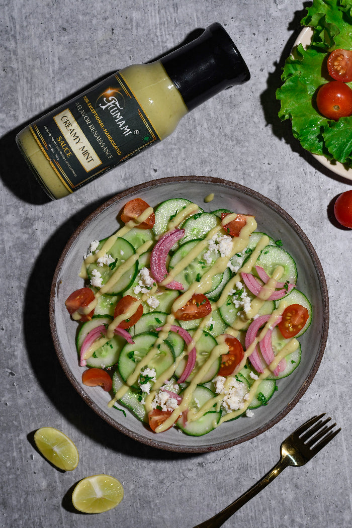 Delicious salad with cucumbers, tomatoes, and onions and feta cheese drizzled with a Fumami fermented creamy mint sauce, next to a bottle of Creamy Mint.