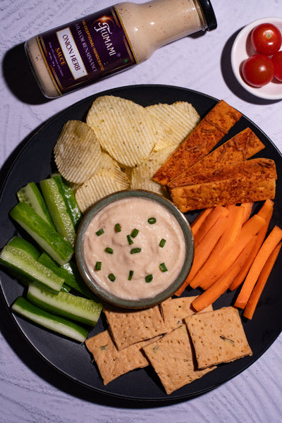 Platter of chips, vegetables, and crackers with a bowl of Fumami Onion Herb dip, and a bottle of Fumami Onion Herb sauce  in the background.