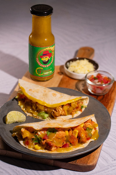 Two tacos on a plate with a bottle of Fumami fermented hot sauce and ingredients in the background.